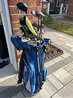 Overall view of the blue Callaway golf bag filled with golf clubs leaning against a wall outside on pavement, showing the condition and fullness of the bag.