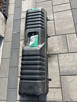 Black hard shell golf case laying on pavement, showing ribbed design and handle compartment with item inside.