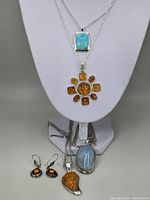 Photo of all jewelry displayed on a white bust including four necklaces with amber, turquoise, aquamarine pendants and one pair of amber earrings