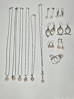Full view of 6 silver chains with pearl pendants, 5 pairs of earrings, and 2 silver and pearl rings.
