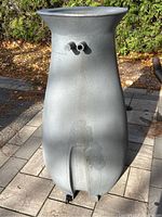 Front view of the gray rain barrel showing the two top spout openings and wear marks on the surface.
