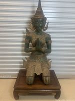 Front view of kneeling Thai Buddhist sculpture in prayer pose on wooden base