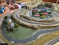 Overview of assembled layout with multiple loops of track, hillside scenery, small town buildings and bridge