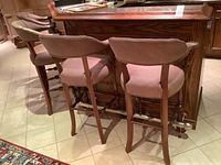 Four matching high wooden bar chairs lined up against a bar counter, showing the overall style and shape, wood tones and upholstery color.
