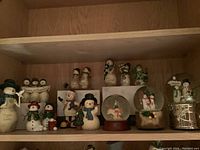 Overview of shelf with various snowman figurines and three snow globes, showing details like clothing and signs
