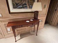 Full view of console table against paneled wall with lamp and two coasters on top