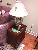 Wide view of the wood side table next to a pink upholstered couch topped with ceramic base lamp with beige shade and decorative candle.