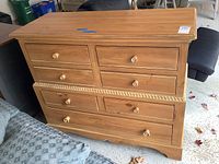 Front view showing seven drawers with wooden knobs, natural finish, carved rope detail above bottom drawer.