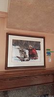 Full view of framed print hanging on wall above fireplace, showing snow scene with person and dog.