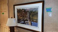 Framed print hanging on wall with a table lamp beside it, showing overall lot condition and setting.