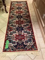 Full view of wool runner rug laid out on tile floor, showing its length, pattern and fringed edge.