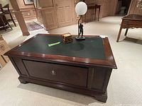 Wide view of the rectangular wood table with dark faux leather insert top and file drawer closed, top showing the lamp and coasters.