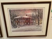 Framed winter scenery print showing a colonial house covered in snow, with trees and lit windows visible.