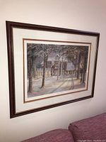 Front view of framed print hanging on a light colored wall, showing the winter house scene.