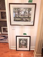 Photo showing two framed prints leaned against wall, one larger on top and smaller below, in a well-lit room with wood flooring