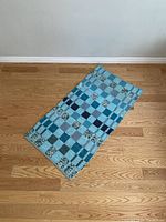Blue rug laid flat on wooden floor, showing patchwork squares in different blue tones and floral patterns.