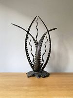 Front view of a Brutalist metal sculpture showing organic, abstract leaf shapes and textured metal finish, standing on a wooden surface.