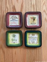 Top view of four square ceramic coasters with vintage wine label designs and colored borders.