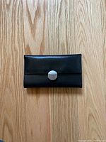 Front view of black leather wallet purse with silver metal clasp on wood floor.