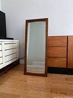 Full view of rectangular teak framed mirror leaning against wall between credenza units