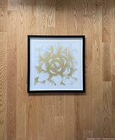 Full view of framed white and gold flower wall art laid on wood floor
