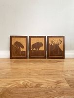 Three wooden plaques displayed side by side showing bear, bison, and stag animal inlays.