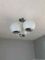 Three white glass globes mounted to chrome frame against ceiling