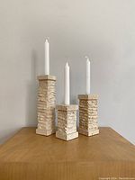 Three travertine candle holders displayed upright with white taper candles, showing overall height and texture.