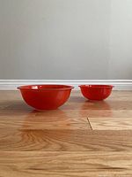 Two red Pyrex mixing bowls placed on wooden floor, showing size comparison and shape.