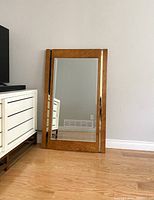 Vintage rectangular mirror with birdseye maple frame and built-in brass strips, propped on floor by white dresser and wood drawer chest.