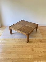 Square vintage wood coffee table with parquet style top and sturdy legs set on light hardwood floor.