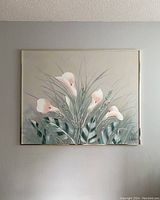 Front view of large oil painting showing floral subject with calla lilies and foliage against a neutral background, framed and hanging on a wall above furniture.