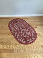 Oval braided rug placed on a wooden floor, showing the overall shape, pattern, and color of the rug.