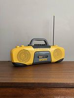 Front angle showing yellow and gray portable cassette player with handle, speaker grills, and tuning dials.