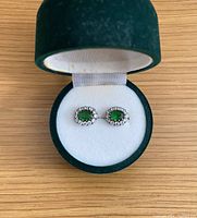 Top view of earrings in green velvet box showing green central stones surrounded by clear accents.
