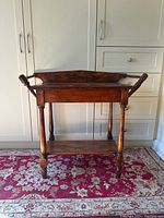 Front view of antique pine washstand showing turned legs, raised edges on the top, and lower shelf.