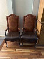 Pair of antique style dining armchairs with carved wood and plaster legs, leather seats, and patterned upholstered backs.