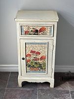 Front view of shabby chic side table showing drawer and door with floral mosaic tile insets.