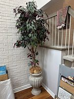 Full shot of tall artificial tree with multicolored leaves, placed in a decorative fibreglass urn with faux cement finish