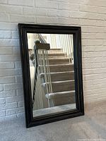 Full front view of the framed mirror against a white brick wall, showing the size and general appearance.