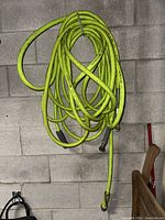 Long lime green flexible garden hose with black reinforced connectors, coiled and hanging against a concrete block wall.