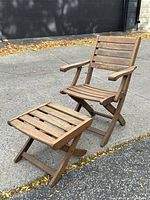Teak rocking lounge chair and matching ottoman side view on pavement outdoors, showing natural weathered wood finish and slatted design.