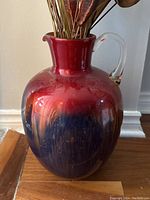 Closeup of the shorter colorful glass vase showing red to dark blue gradient finish and dried decorative foliage inside.