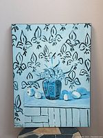 Art print on board showing a blue vase with flowers placed on a white table with round fruits and fleur-de-lis patterned background in black on light blue.