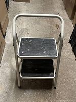 View of lightweight two-step ladder showing top step and safety handle with stains on step surfaces