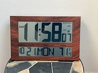 Front view of the oversized digital clock showing time, date, day, and temperature with simulated rosewood finish frame.