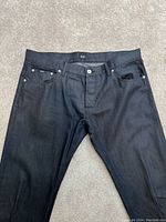 Front view of black Hugo Boss jeans showing button closure, pockets, and overall straight fit style on carpeted floor.