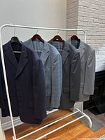 Four men's tailor made suit jackets on rack: navy blue, light blue plaid, dark grey, light grey.