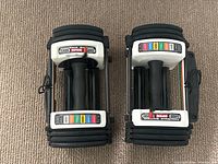 Top view of two PowerBlock Urethane adjustable dumbbells side by side on carpet.