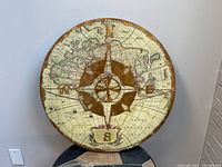 Full view of the round wall hanging with visible map and gold compass in center.